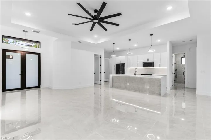 Unfurnished living room with ceiling fan, a raised ceiling, french doors, and sink