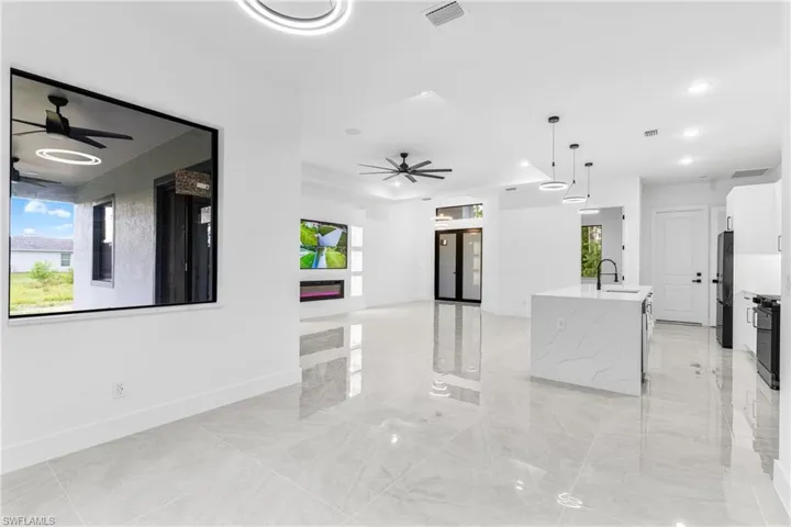 Kitchen with sink, an island with sink, black appliances, decorative light fixtures, and light stone countertops
