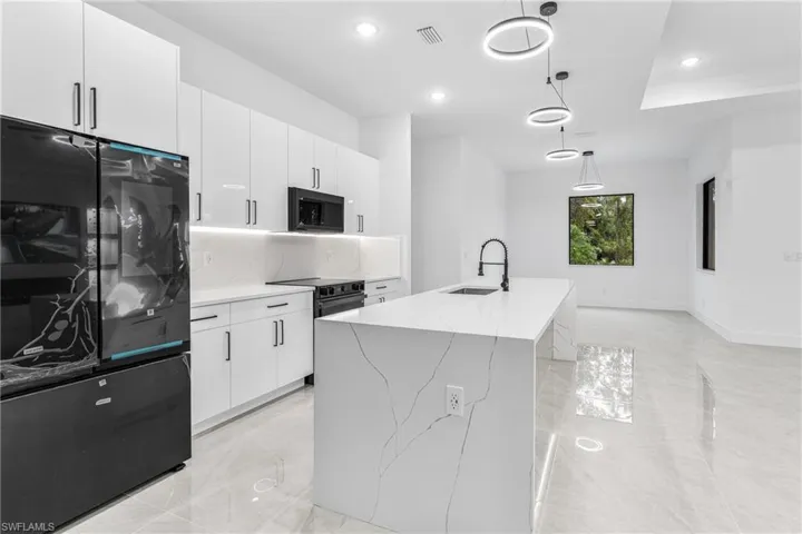Kitchen with pendant lighting, sink, white cabinetry, black appliances, and a center island with sink