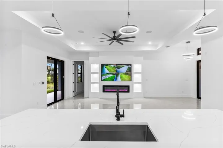 Kitchen with hanging light fixtures, light stone countertops, sink, and a raised ceiling