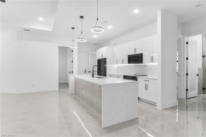 Kitchen featuring white cabinetry, decorative light fixtures, black refrigerator, and a kitchen island with sink