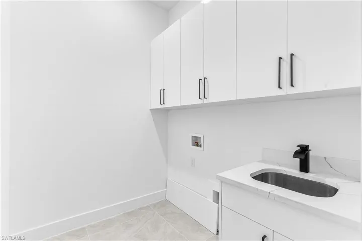 Washroom featuring light tile patterned floors, sink, washer hookup, and cabinets