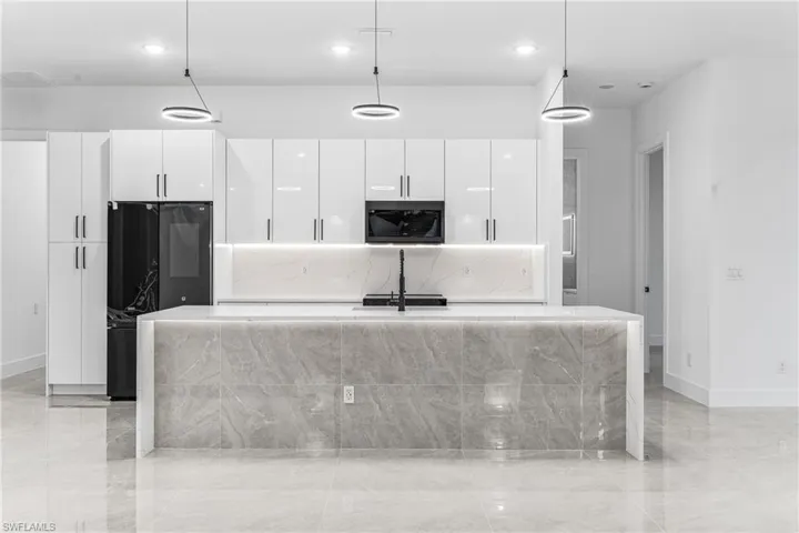 Kitchen featuring white cabinetry, an island with sink, and decorative light fixtures