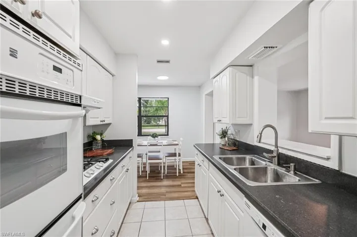 Kitchen with dark countertops, light tile patterned floors, white cabinets, recessed lighting, and white appliances