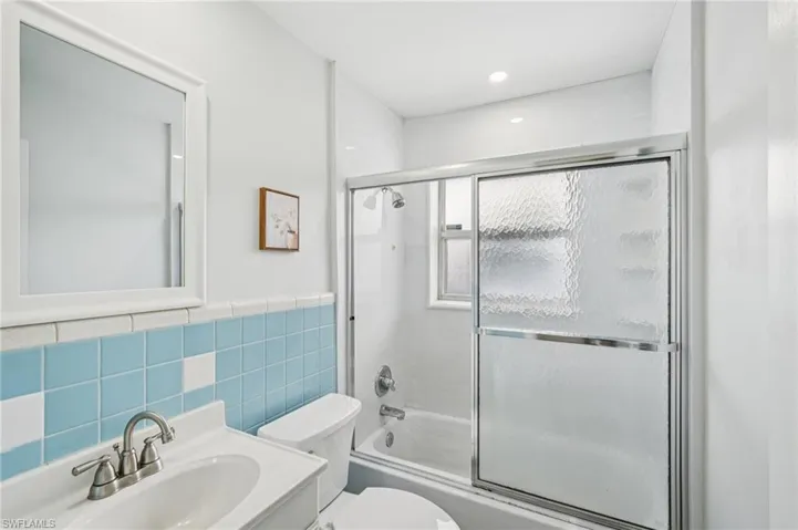 Full bathroom featuring shower / bath combination with glass door, vanity, tile walls, and recessed lighting