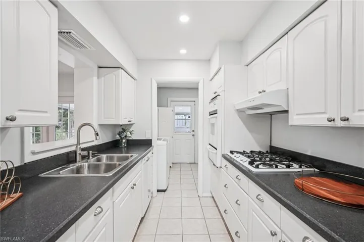 Kitchen featuring white cabinets, healthy amount of natural light, light tile patterned floors, white appliances, and recessed lighting