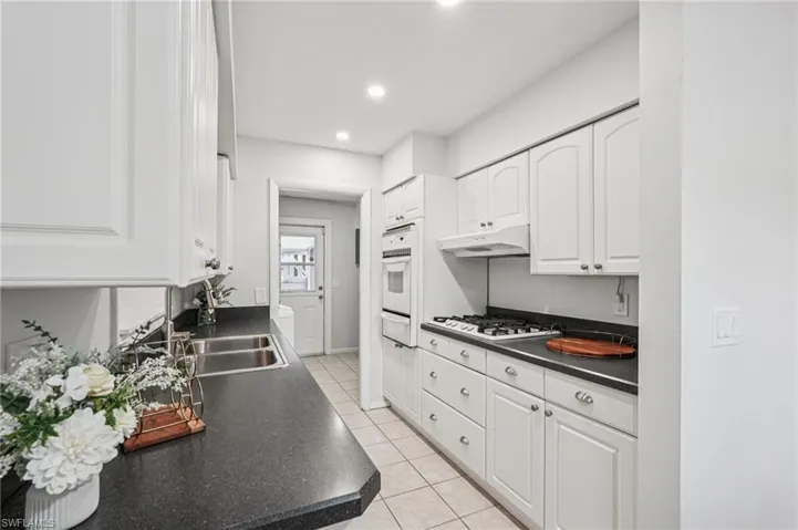 Kitchen with dark countertops, white cabinetry, light tile patterned floors, recessed lighting, and white oven