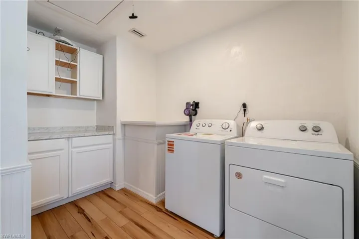 Laundry area with washing machine and clothes dryer, light wood-style floors, cabinet space, and a wainscoted wall