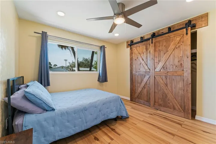 Bedroom featuring light wood-style flooring, a ceiling fan, a barn door, and recessed lighting