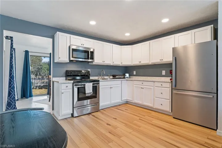 Kitchen with stainless steel appliances, white cabinets, light wood-style flooring, and recessed lighting
