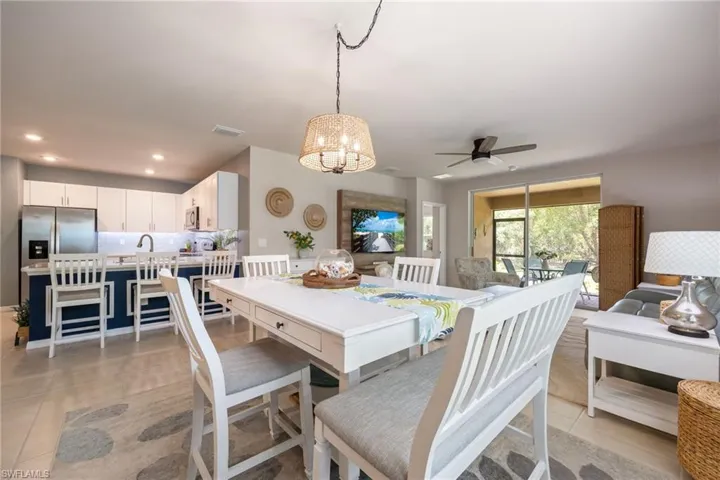Open concept living area featuring a central dining table, a kitchen with white cabinetry and stainless steel appliances, and a screened patio