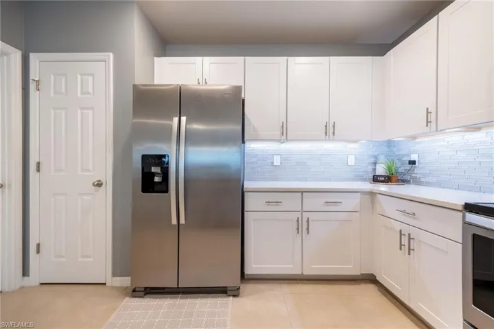 Modern kitchen featuring white shaker cabinetry, stainless steel side-by-side refrigerator, light-colored countertops, and a blue subway tile backsplash with under-cabinet lighting