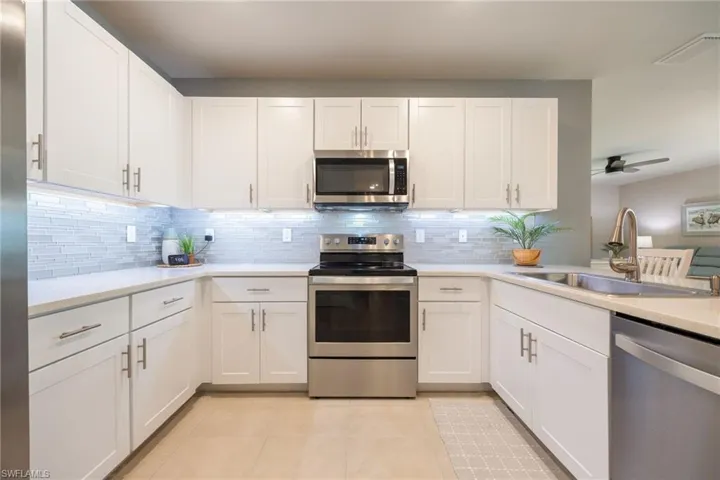 U-shaped kitchen featuring white shaker cabinetry, stainless steel appliances, a tile backsplash, and light-toned countertops