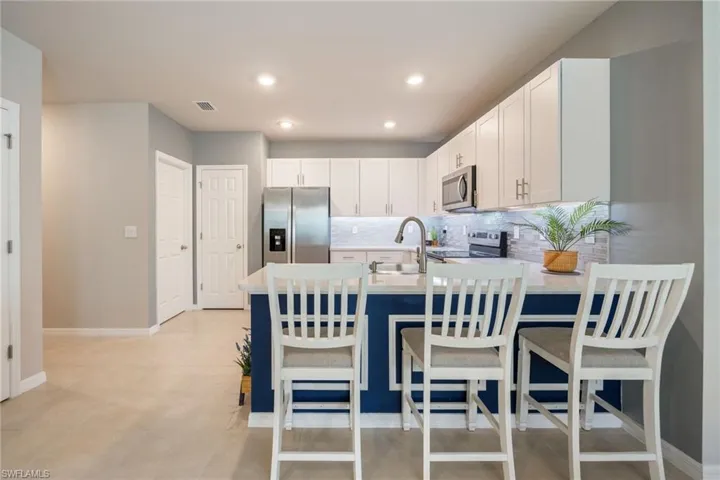 Modern kitchen featuring a blue accent island with seating, white shaker-style cabinetry, stainless steel appliances, a tiled backsplash, and recessed lighting