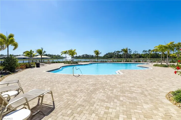 Expansive outdoor pool area featuring a freeform swimming pool, extensive paver decking, and mature palm trees