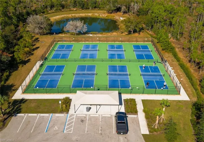 Eight pickleball courts with perimeter fencing, a covered entrance area, and an asphalt parking lot