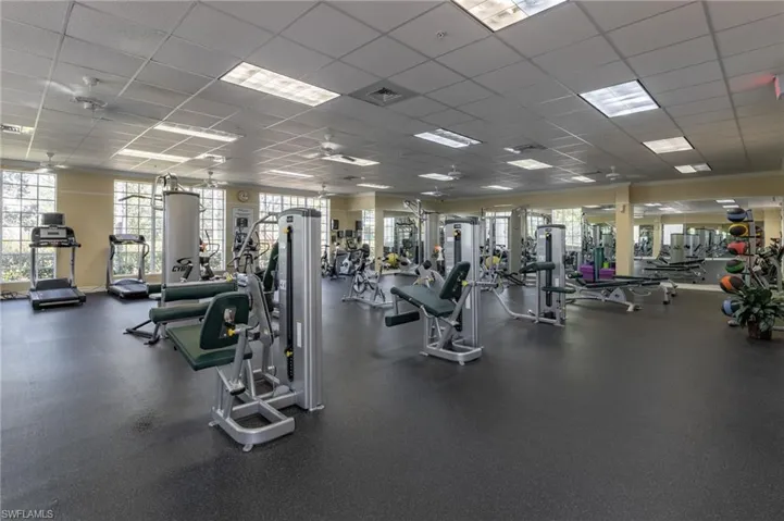 Spacious fitness center featuring robust exercise equipment, extensive rubberized flooring, abundant natural light from multiple windows, recessed ceiling lighting, and multiple ceiling fans