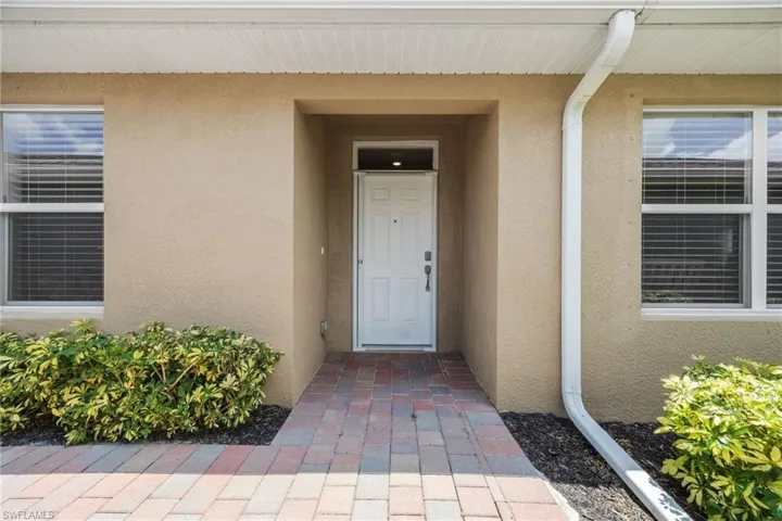 Recessed entry featuring a white paneled door, complemented by a paver walkway and shrubbery plantings