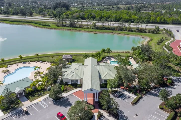 Community clubhouse featuring a covered entry, two outdoor pools, a dedicated parking area, and a large lake