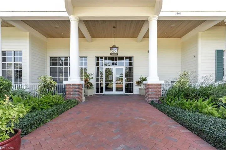 Columned entry featuring a brick paver walkway, wood-finish ceiling, and professional landscaping