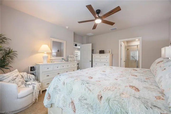 Carpeted room featuring a ceiling fan with integrated lighting, neutral wall tones, and a doorway leading to a bathroom with a glass-enclosed shower