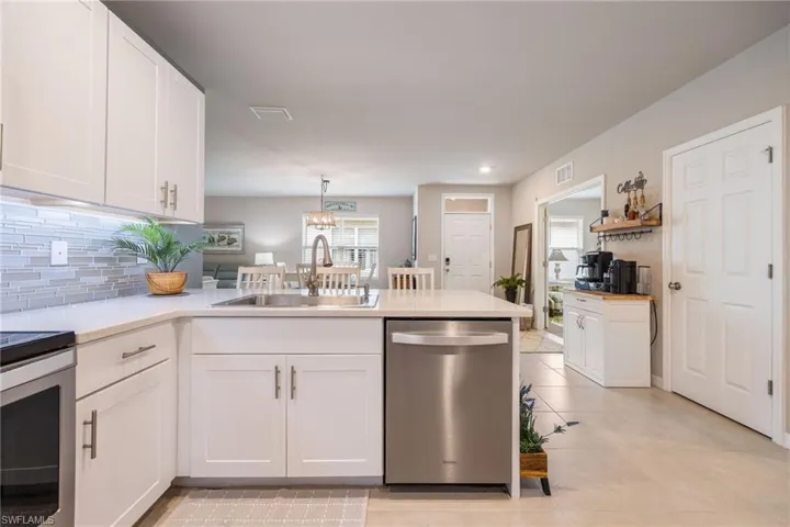 Modern kitchen featuring white shaker cabinetry, stainless steel appliances, a tiled backsplash, a kitchen island with an undermount sink, and light-toned countertops