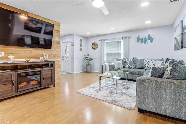 Living room with light wood-type flooring, a ceiling fan, recessed lighting, a textured ceiling, and baseboards