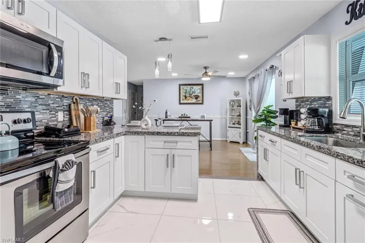 Kitchen featuring appliances with stainless steel finishes, a sink, a peninsula, white cabinetry, and recessed lighting