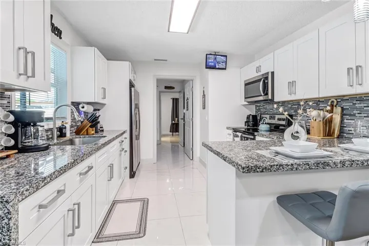 Kitchen featuring appliances with stainless steel finishes, stone counters, a sink, backsplash, and white cabinets