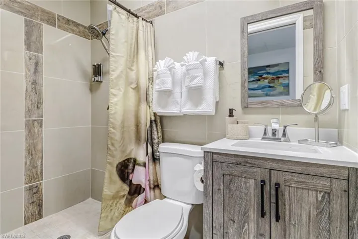 Bathroom featuring toilet, a tile shower, tile walls, and vanity