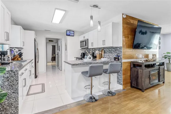 Kitchen with stainless steel appliances, a sink, light stone counters, tasteful backsplash, and white cabinets