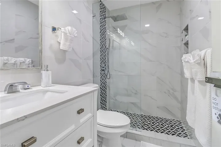 Bathroom featuring a walk in shower, vanity, tile walls, and toilet