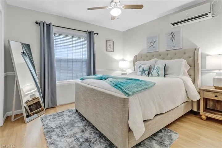 Bedroom featuring an AC wall unit, light wood-style flooring, and ceiling fan