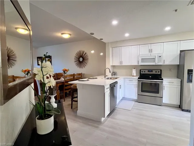 Kitchen featuring stainless steel appliances, a peninsula, white cabinetry, a kitchen breakfast bar, and light wood-style floors