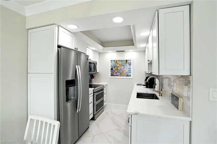 Kitchen featuring stainless steel appliances, white cabinets, light stone counters, backsplash, and recessed lighting