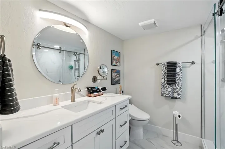 Bathroom featuring vanity, a marble finish shower, and light marble finish flooring