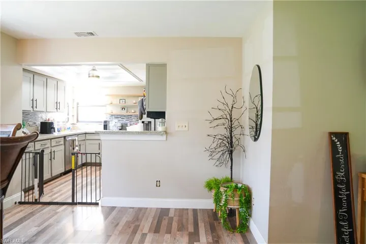 Modern kitchen with pass-through opening to an adjacent room, featuring light gray cabinetry, a mosaic tile backsplash, and light-tone countertops