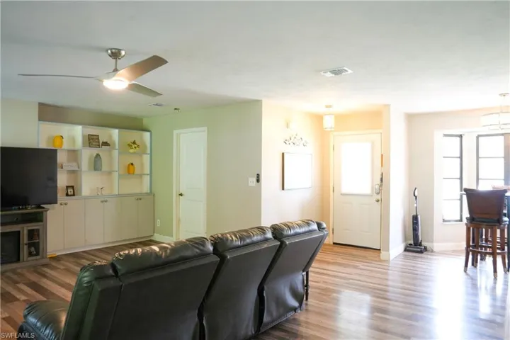 Spacious living area featuring wood-finish flooring, a built-in media center with open shelving and cabinetry, and a modern ceiling fan with integrated lighting