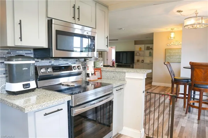 Kitchen featuring granite countertops, stainless steel appliances including a range and microwave, light cabinetry with dark hardware, and a mosaic tile backsplash