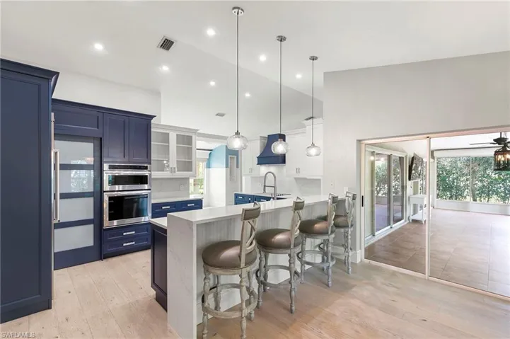 Kitchen with blue cabinets, a peninsula, a kitchen bar, light countertops, and glass insert cabinets