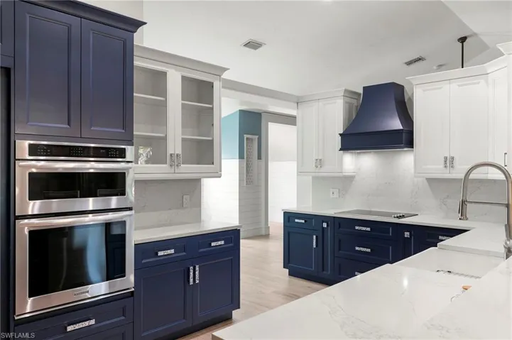 Kitchen featuring double oven, blue cabinets, custom exhaust hood, and light stone countertops