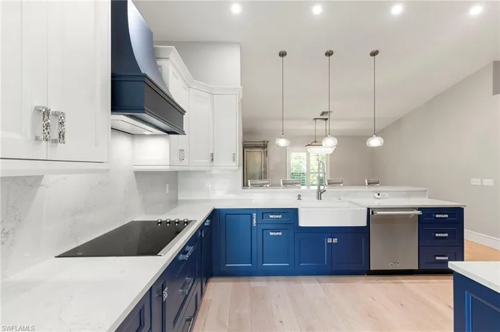 Kitchen with blue cabinets, a peninsula, light wood-type flooring, custom exhaust hood, and white cabinetry