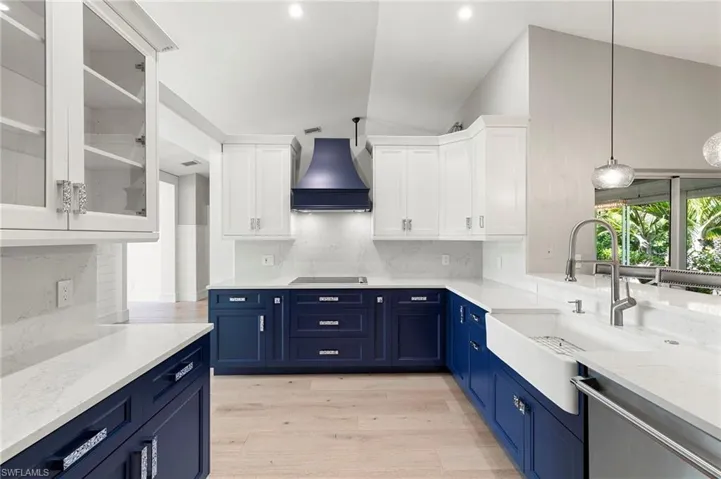 Kitchen with tasteful backsplash, blue cabinetry, lofted ceiling, stainless steel dishwasher, and premium range hood