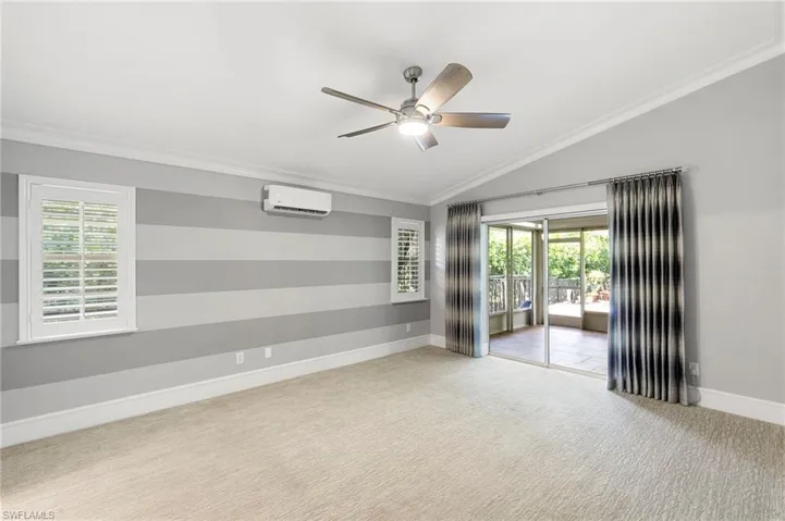 Carpeted spare room featuring vaulted ceiling, ornamental molding, a ceiling fan, and an AC wall unit