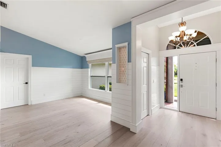 Entryway with wood finished floors, lofted ceiling, a chandelier, and a wainscoted wall