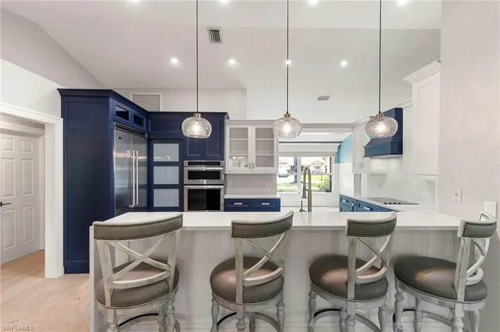 Kitchen featuring blue cabinets, light countertops, glass insert cabinets, appliances with stainless steel finishes, and a peninsula