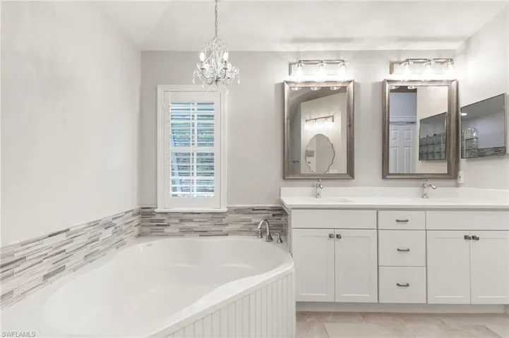 Full bath featuring double vanity, a garden tub, lofted ceiling, and a chandelier