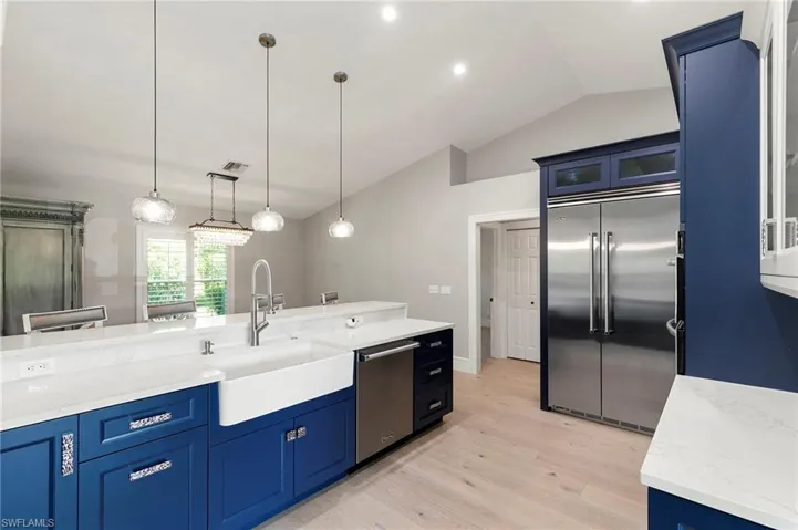 Kitchen with stainless steel appliances, blue cabinetry, light wood finished floors, lofted ceiling, and decorative light fixtures