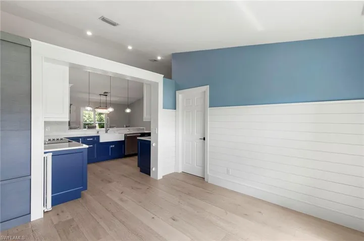 Kitchen featuring light wood-type flooring, blue cabinetry, light countertops, decorative light fixtures, and a peninsula