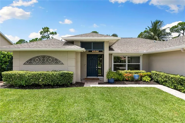 View of exterior entry with stucco siding, a shingled roof, and a yard